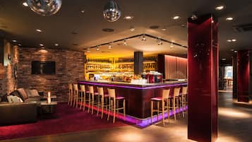 Una zona de bar con una barra larga, varios taburetes y un fondo de pared de ladrillo.