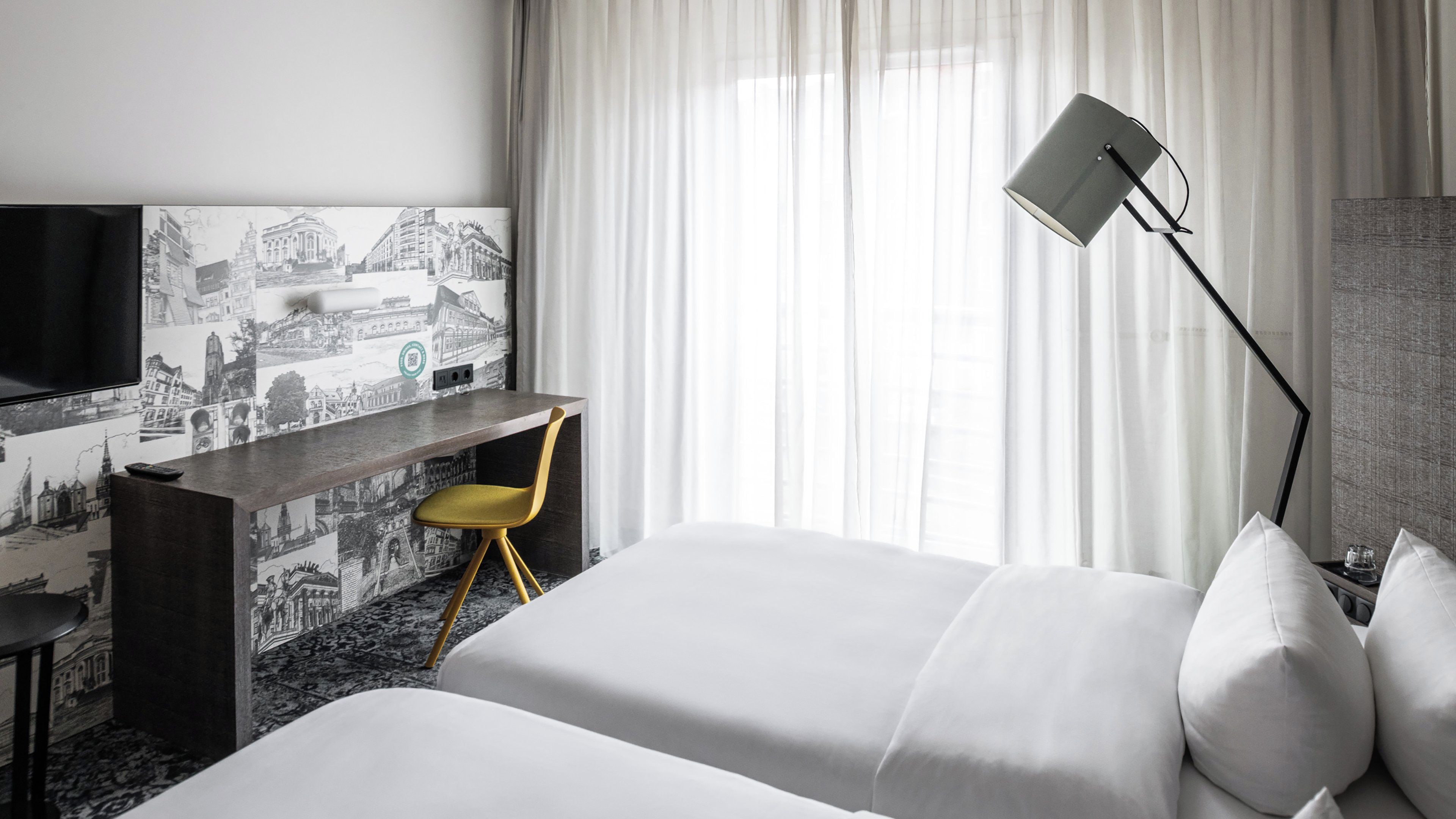 Habitación de hotel con cama, escritorio, silla, televisor y ventana con cortinas.