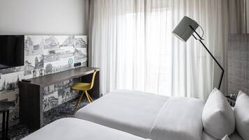 Ein Hotelzimmer mit Bett, Schreibtisch, Stuhl, Fernseher und einem Fenster mit Vorhängen.