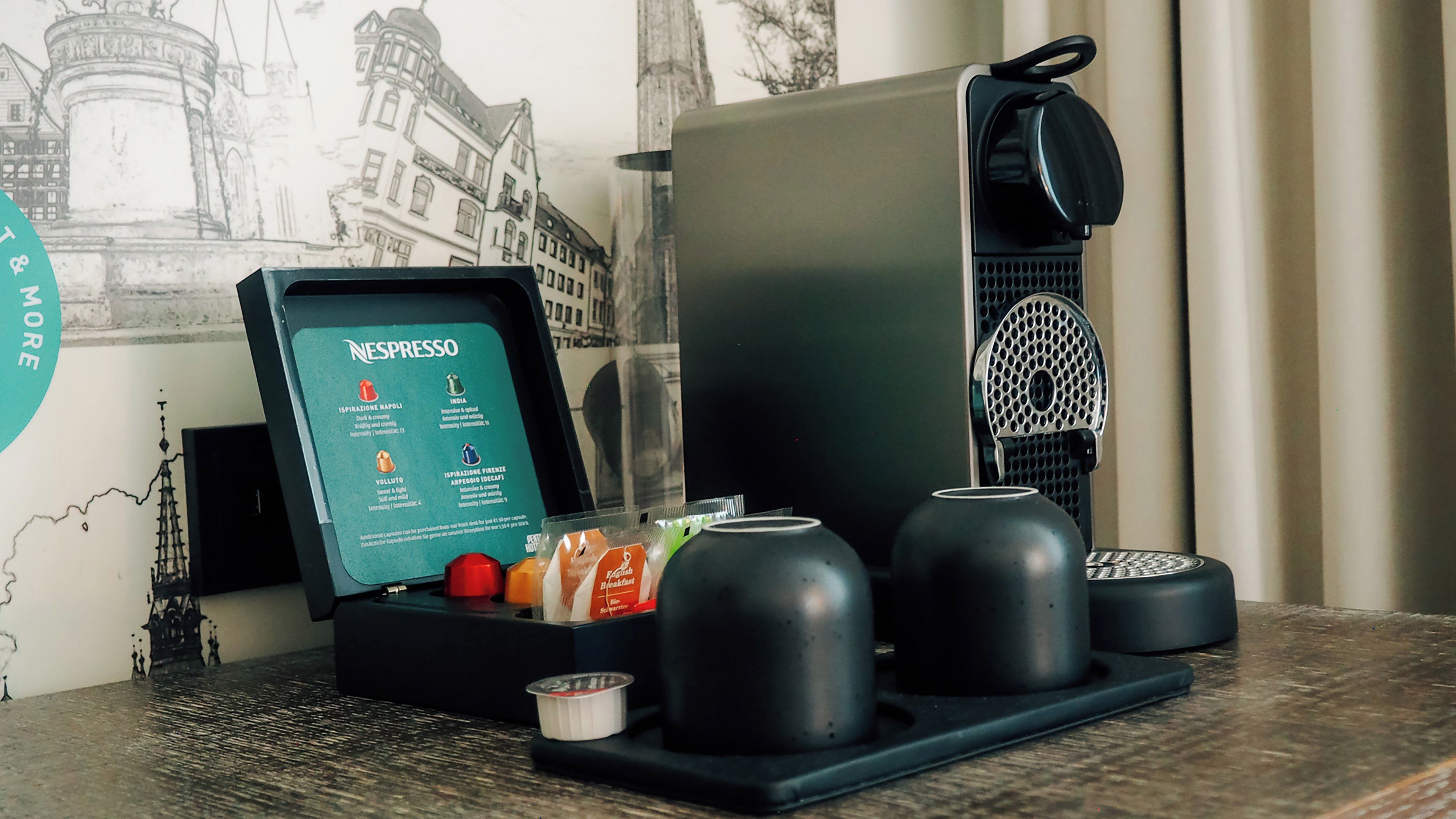 Una cafetera Nespresso con un menú, una taza y un cuenco pequeño sobre una mesa.