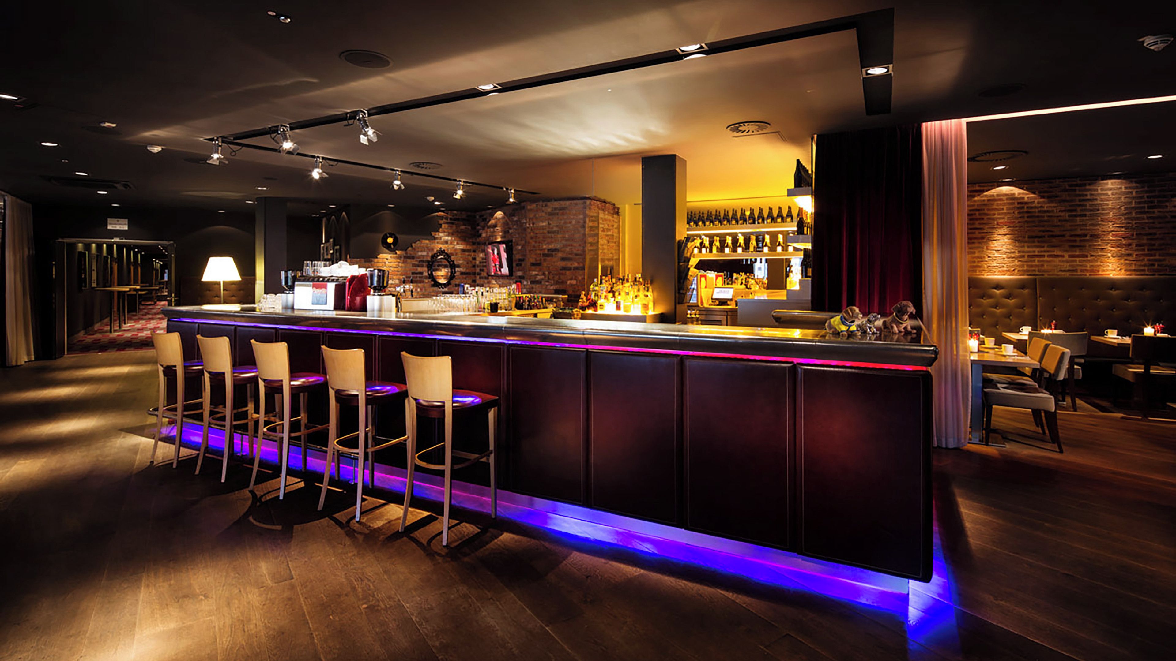 A bar area with a long counter, multiple stools, and a brick wall backdrop.