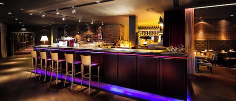 Una zona de bar con una barra larga, varios taburetes y un fondo de pared de ladrillo.