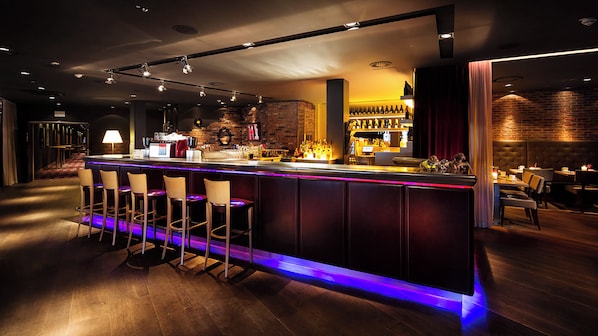 A bar area with a long counter, multiple stools, and a brick wall backdrop. - Pentahotel Braunschweig (Braunschweig)