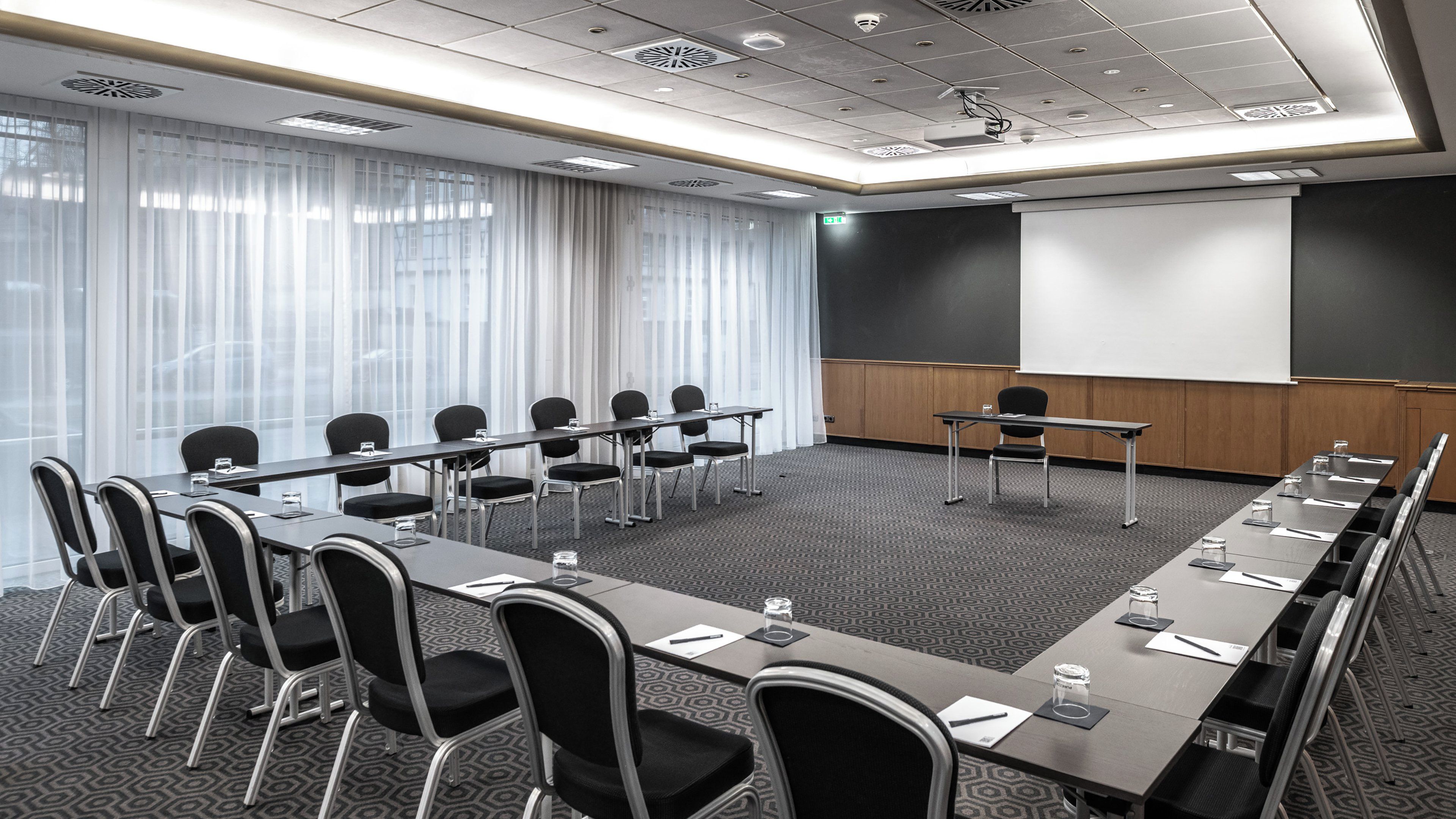 A conference room with a long table, chairs, a projector screen, and a whiteboard.