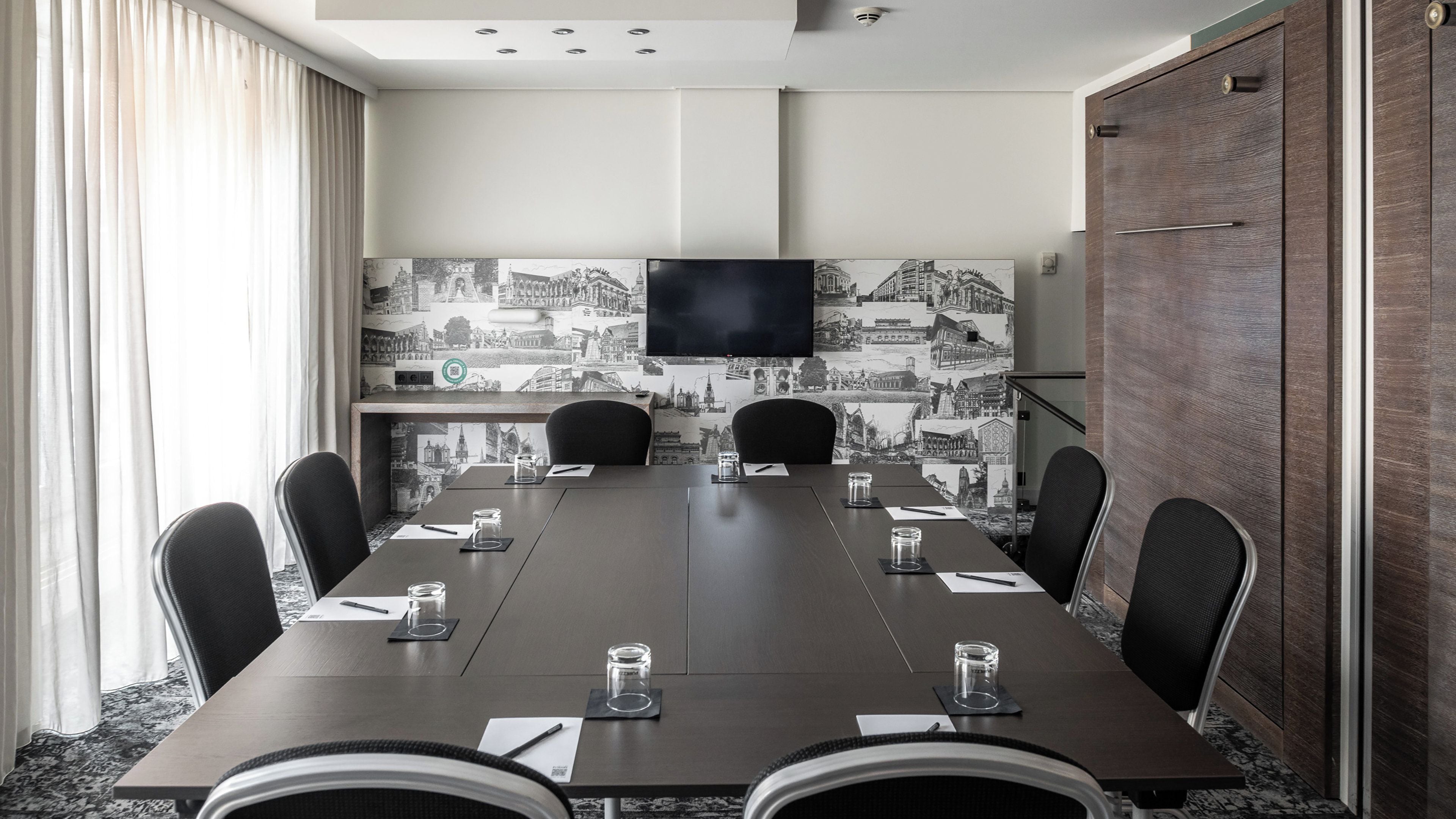 A conference room with a long table, six chairs, a flat-screen TV, and a cityscape wallpaper.