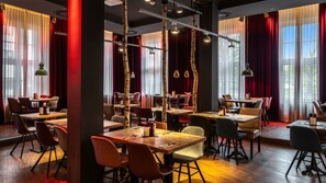 A restaurant interior with wooden tables, chairs, and hanging pendant lights. - Pentahotel Braunschweig (Braunschweig)