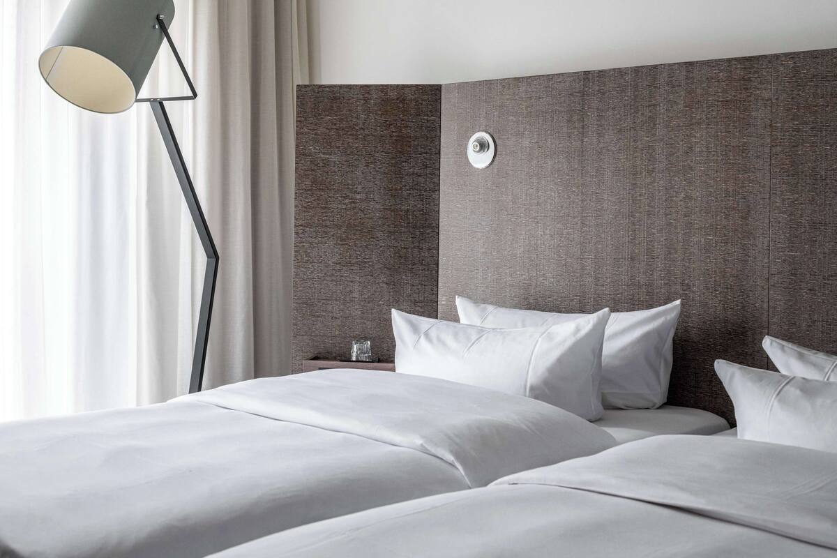 Una habitación de hotel moderna con una cama grande, una mesita de noche con lámpara y un cabecero con textura.