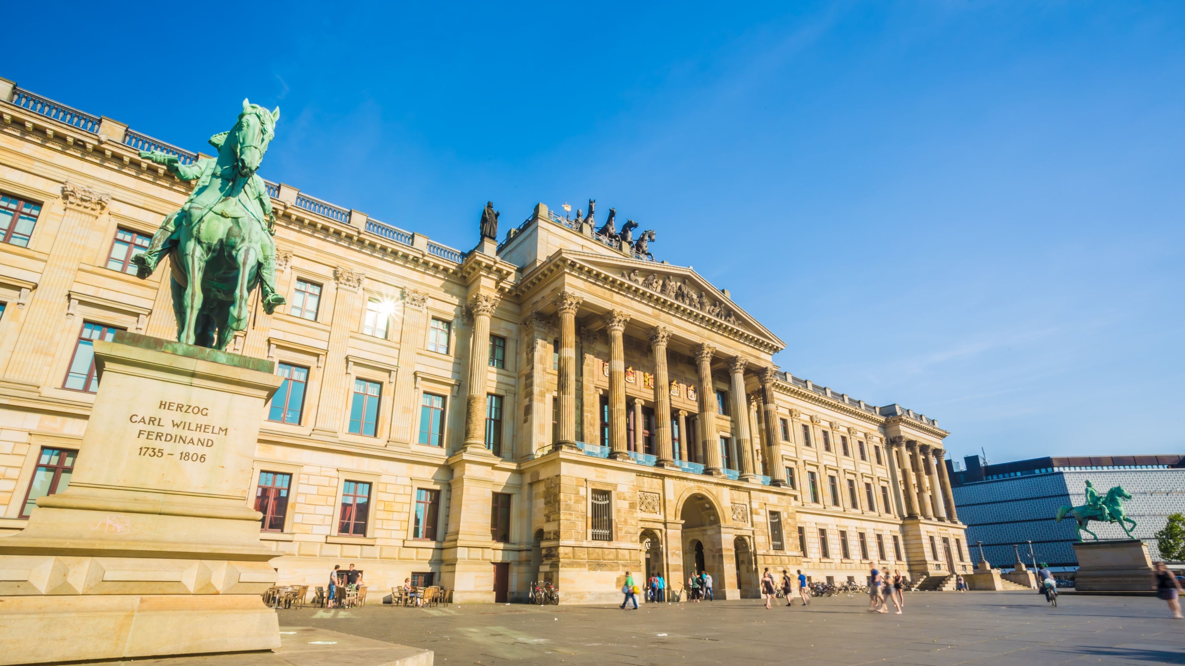 A historic building with classical architecture, including columns and statues, and a statue of a man on horseback.