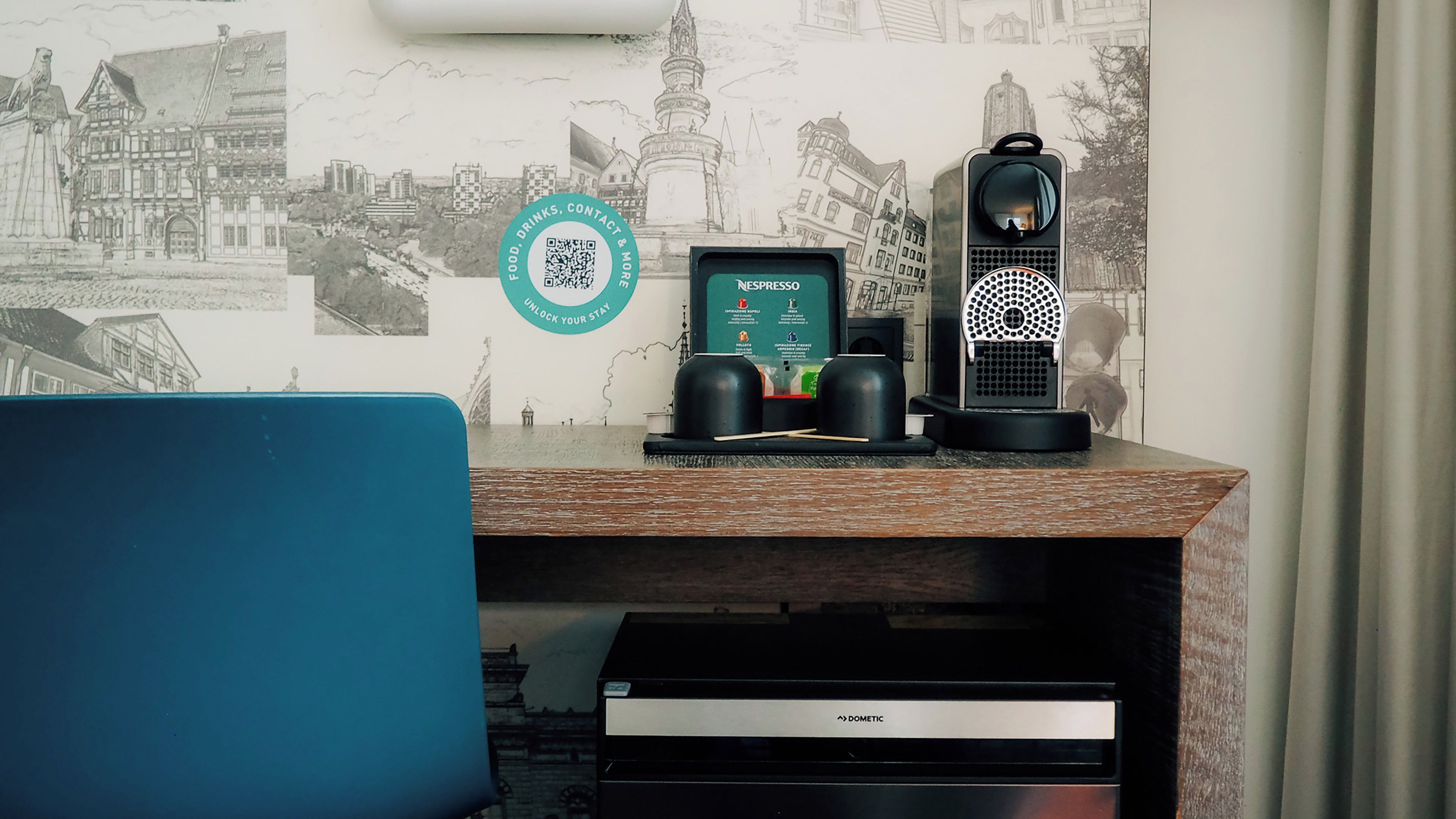 A desk with a Nespresso coffee machine, a smartphone, and a QR code for unlocking a stay.
