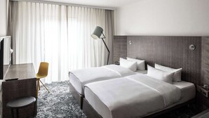 A hotel room with two beds, a desk, a chair, a lamp, and a TV. - pentahotel Braunschweig (Braunschweig)