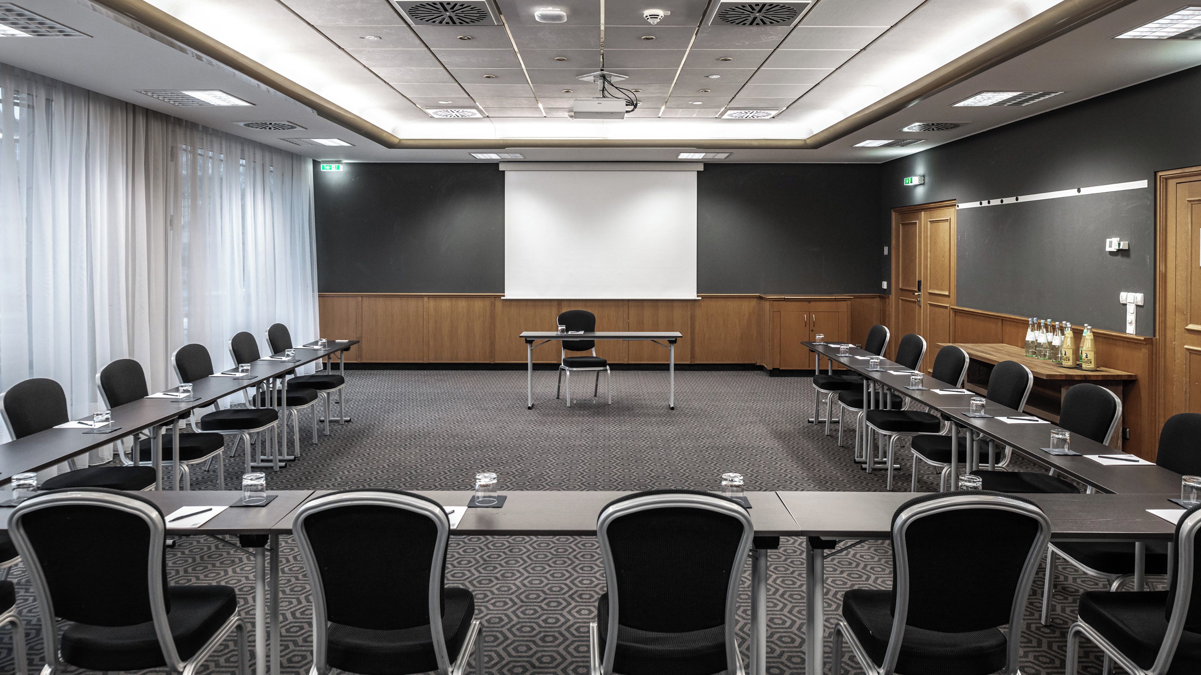 A conference room with a projector screen, a podium, and a row of chairs.