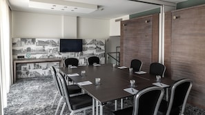 A conference room with a long table, chairs, a flat-screen TV, and a cityscape wallpaper. - Pentahotel Braunschweig (Braunschweig)