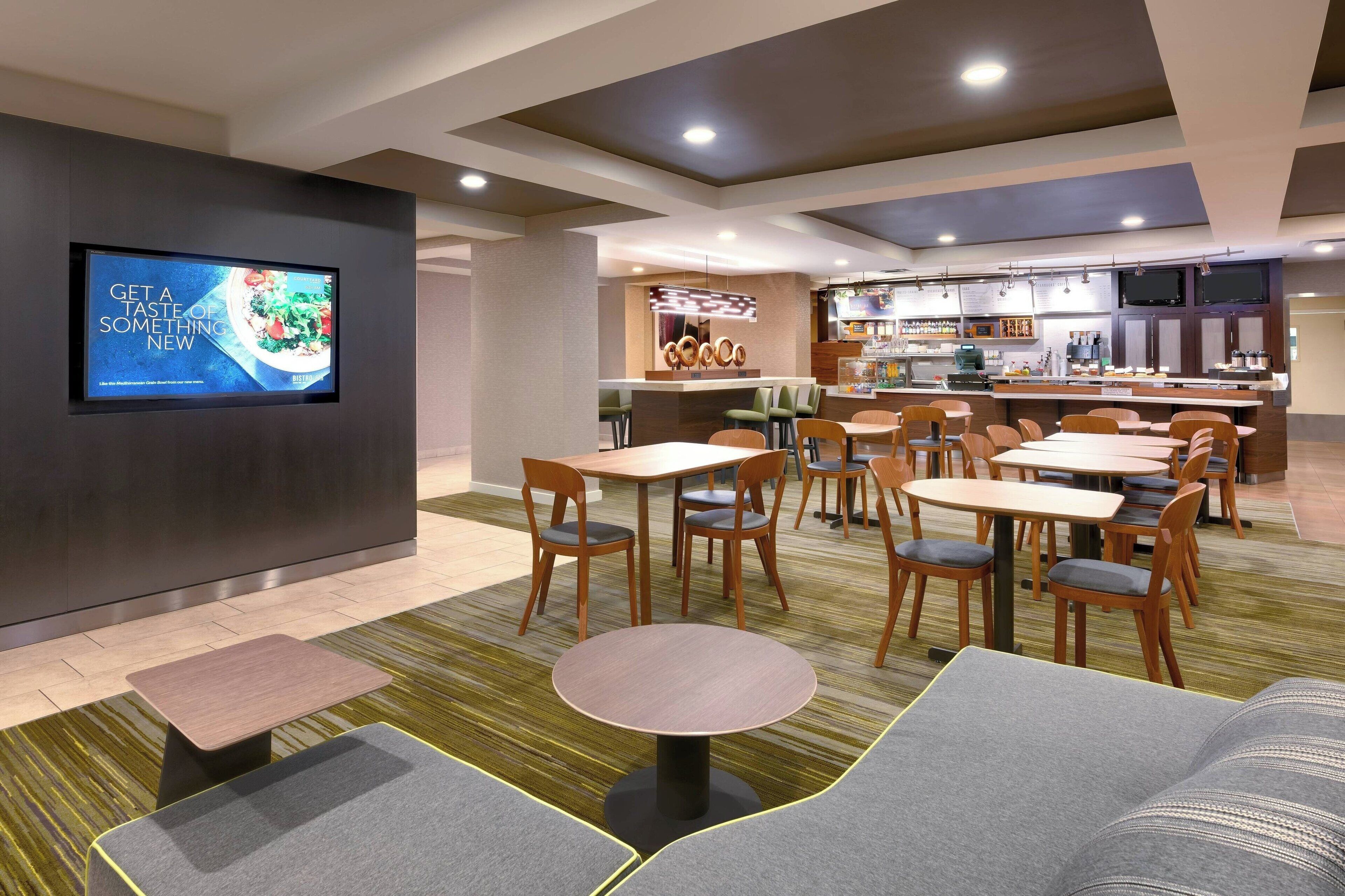 A modern hotel lobby with a TV displaying a menu, a bar area, and seating arrangements.