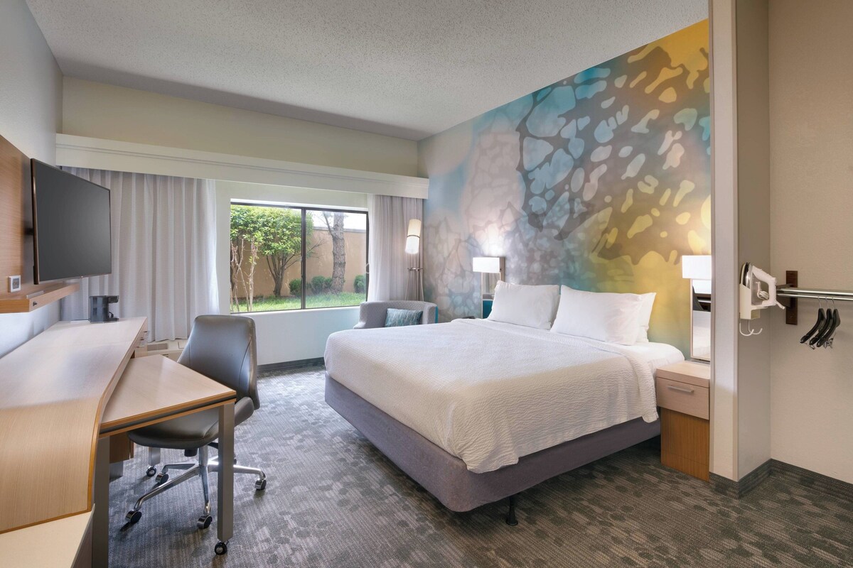 A hotel room with a bed, desk, chair, and a large window.