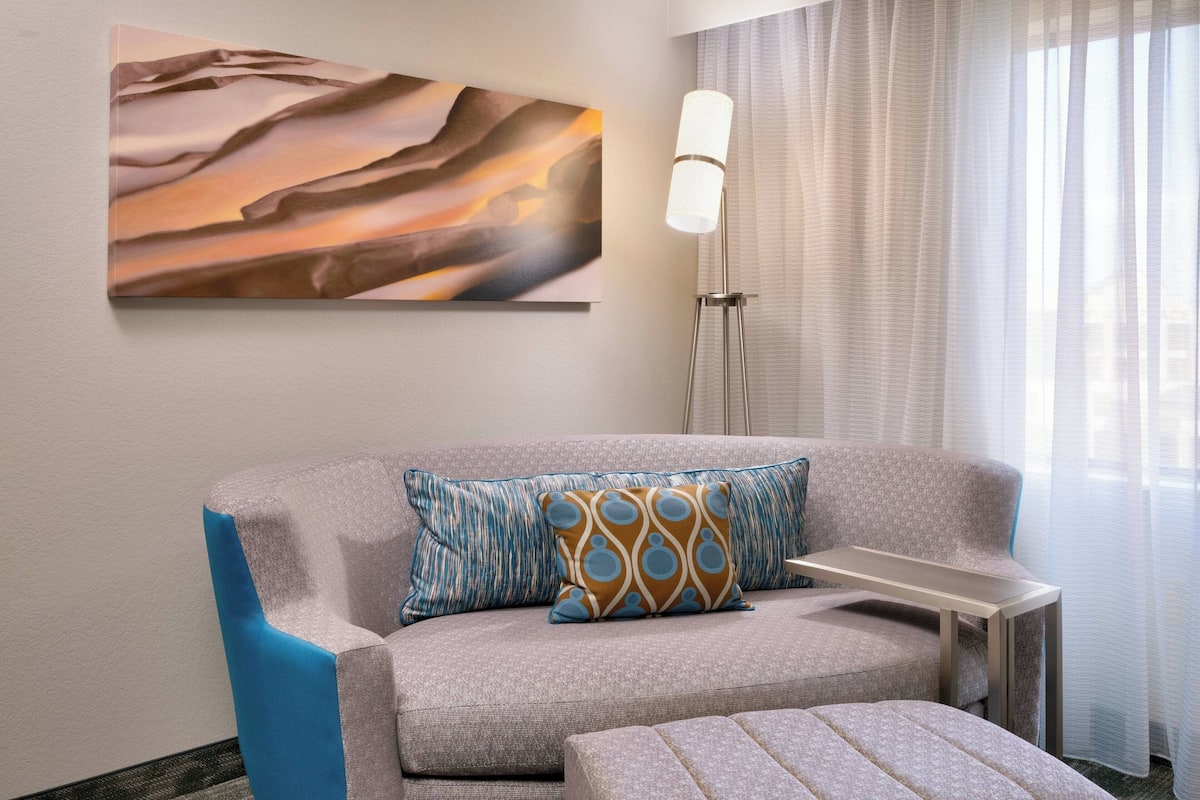 Una habitación moderna con un sofá gris, un cojín estampado, una mesita auxiliar y un cuadro con formas abstractas en la pared.