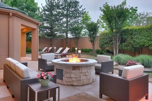 An outdoor patio with a stone fire pit surrounded by wicker furniture and a lounge area with chairs. - Courtyard by Marriott Oklahoma City Northwest (Oklahoma City)