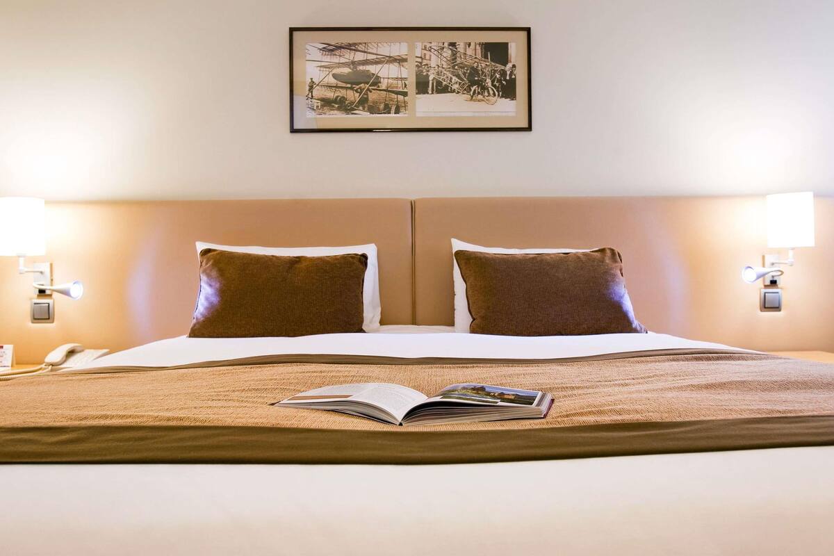 Habitación de hotel con una cama grande, dos almohadas, un cuadro enmarcado en la pared y lámparas de noche.