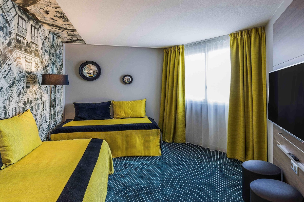 Una habitación de hotel con dos camas, un televisor grande y un papel tapiz estampado.