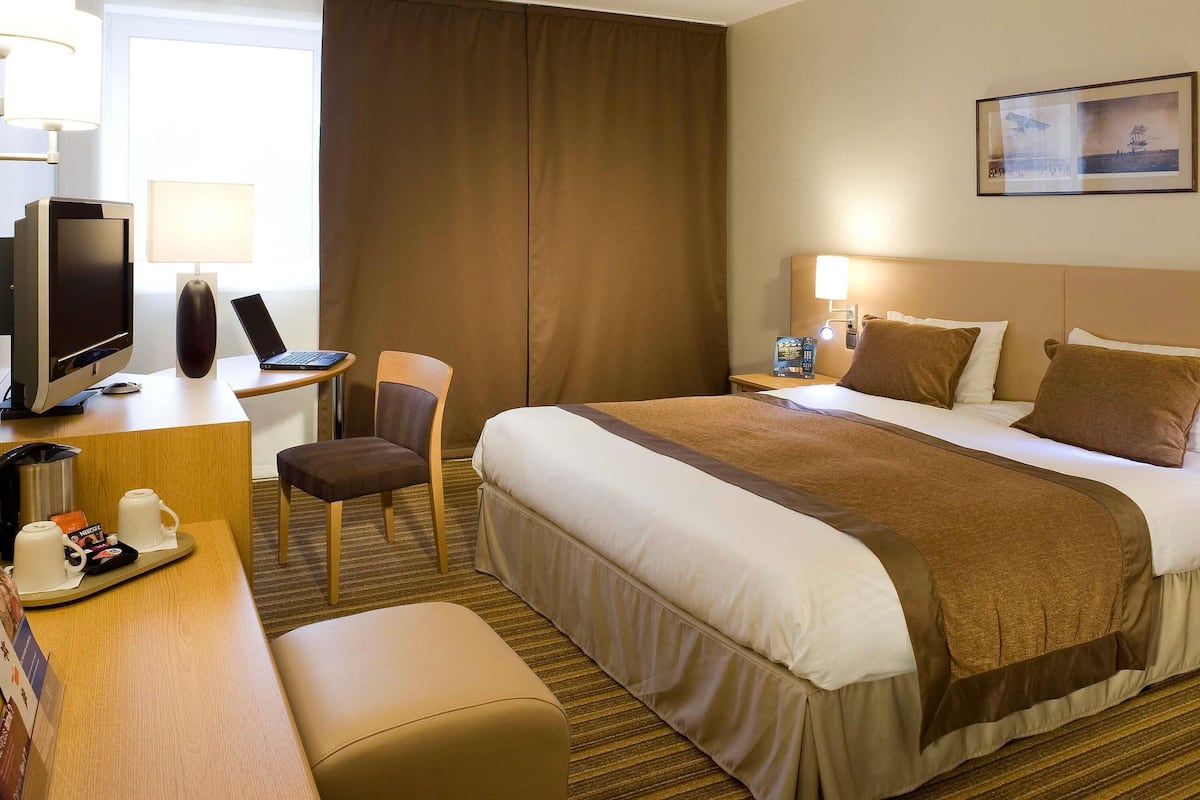 Una habitación de hotel con cama, escritorio, silla, televisor y un cuadro en la pared.