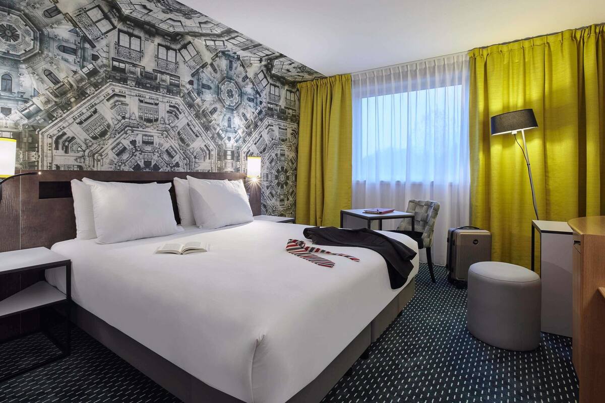 Una habitación de hotel con una cama grande, un escritorio, una silla, una mesita y una lámpara.
