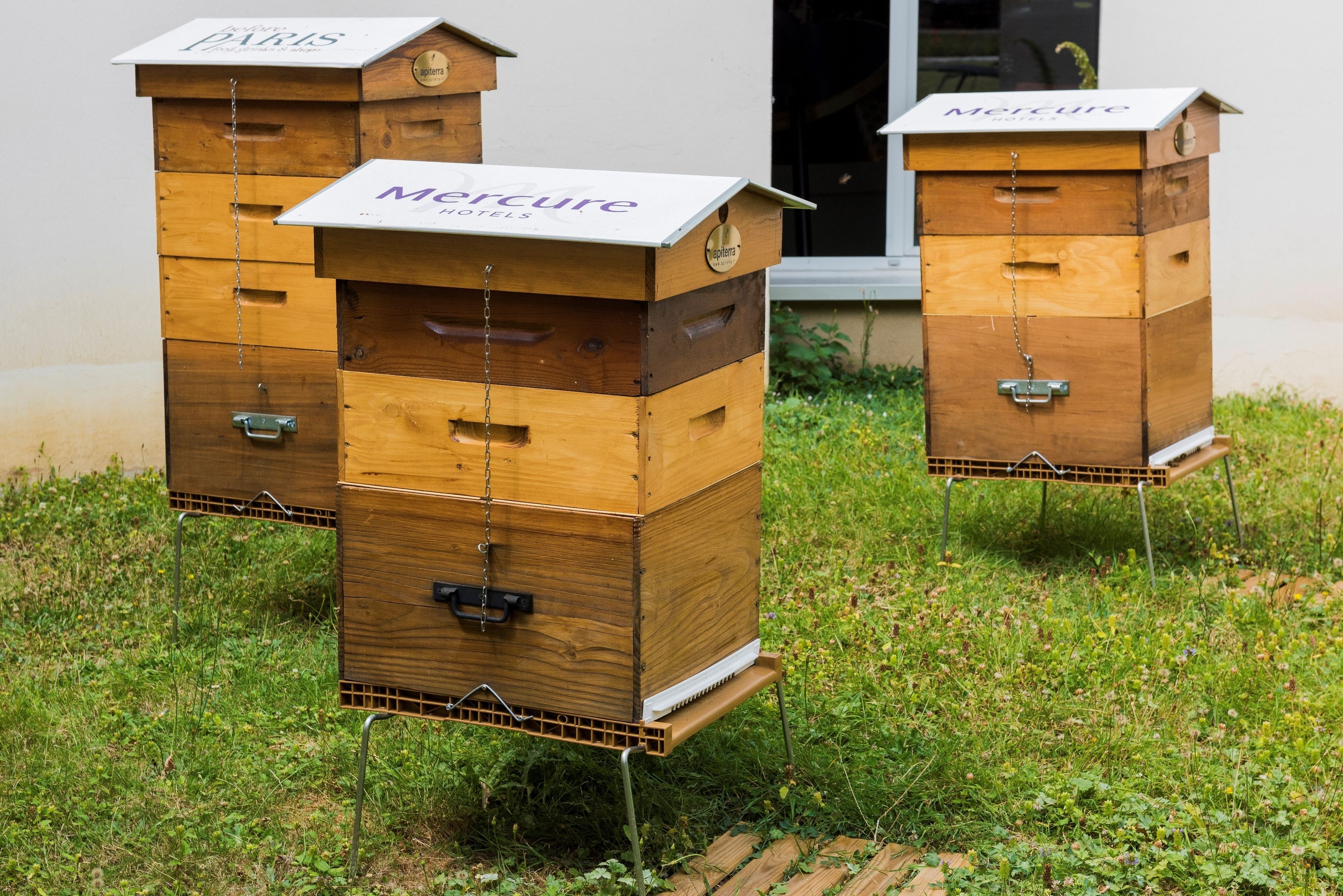 Two wooden beehive structures with 'Mercure Hotels' branding, placed outdoors on grass.