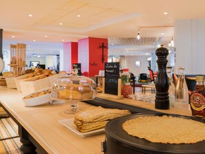 Zona de bufé con diversos alimentos, entre ellos pasteles y un plato grande redondo, posiblemente panqueques o crepes, sobre una mesa de madera.