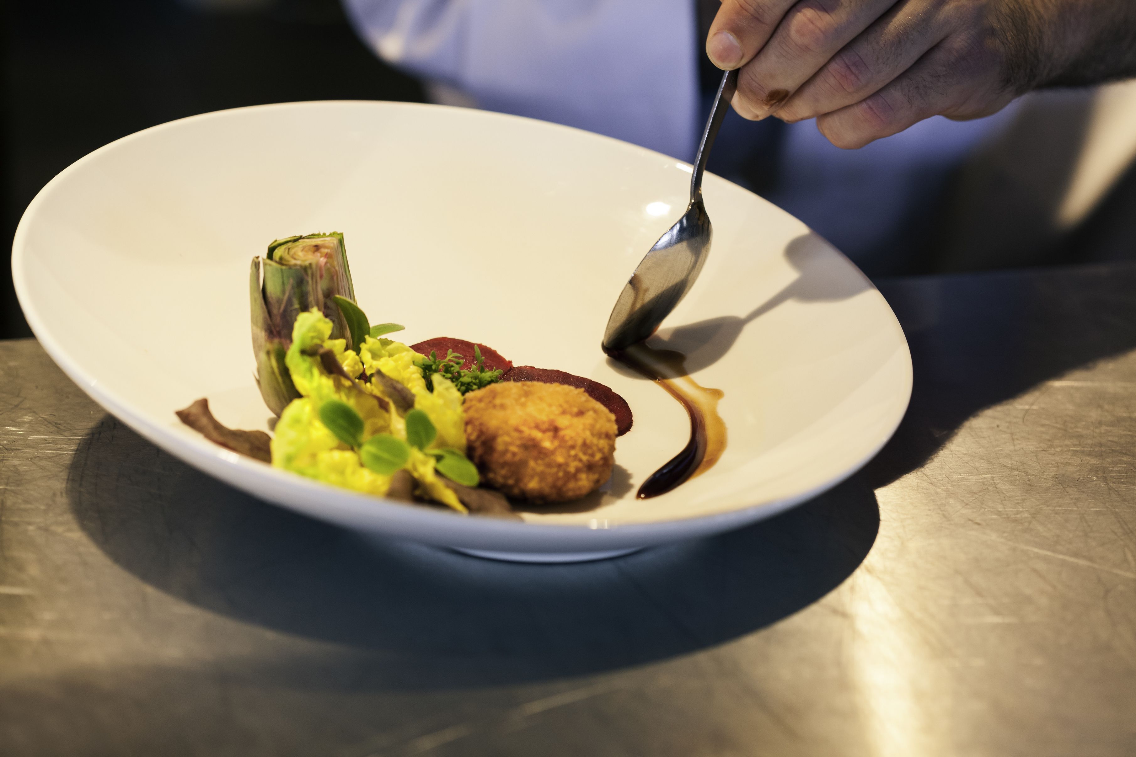 A white plate with a variety of food items, including a piece of meat, a vegetable, and a small round item, on a table.