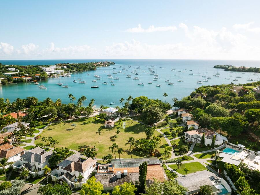Un complejo turístico frente al mar con varias edificaciones, un puerto deportivo lleno de barcos y abundante vegetación.