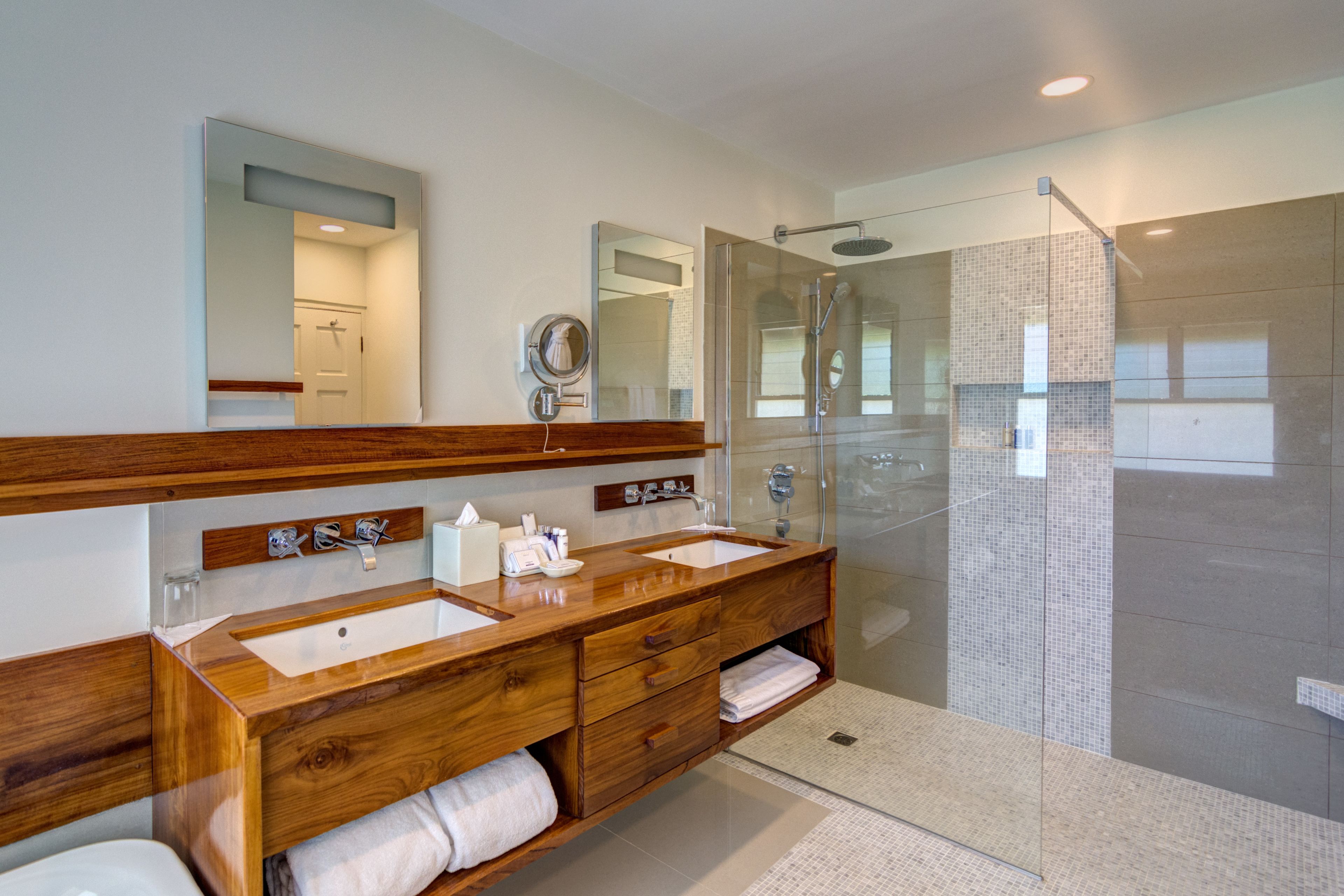 Un baño moderno con tocador de madera, lavamanos dobles, cabina de ducha de vidrio y un espejo grande.