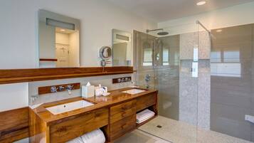 Un baño moderno con tocador de madera, lavamanos dobles, cabina de ducha de vidrio y un espejo grande.