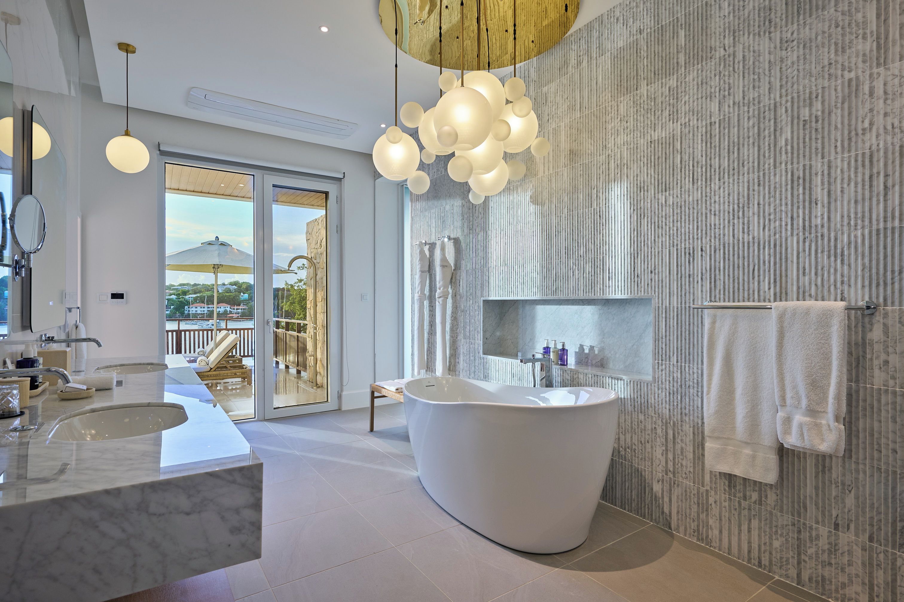 A modern bathroom with a freestanding bathtub, a large mirror, and a view of a balcony.