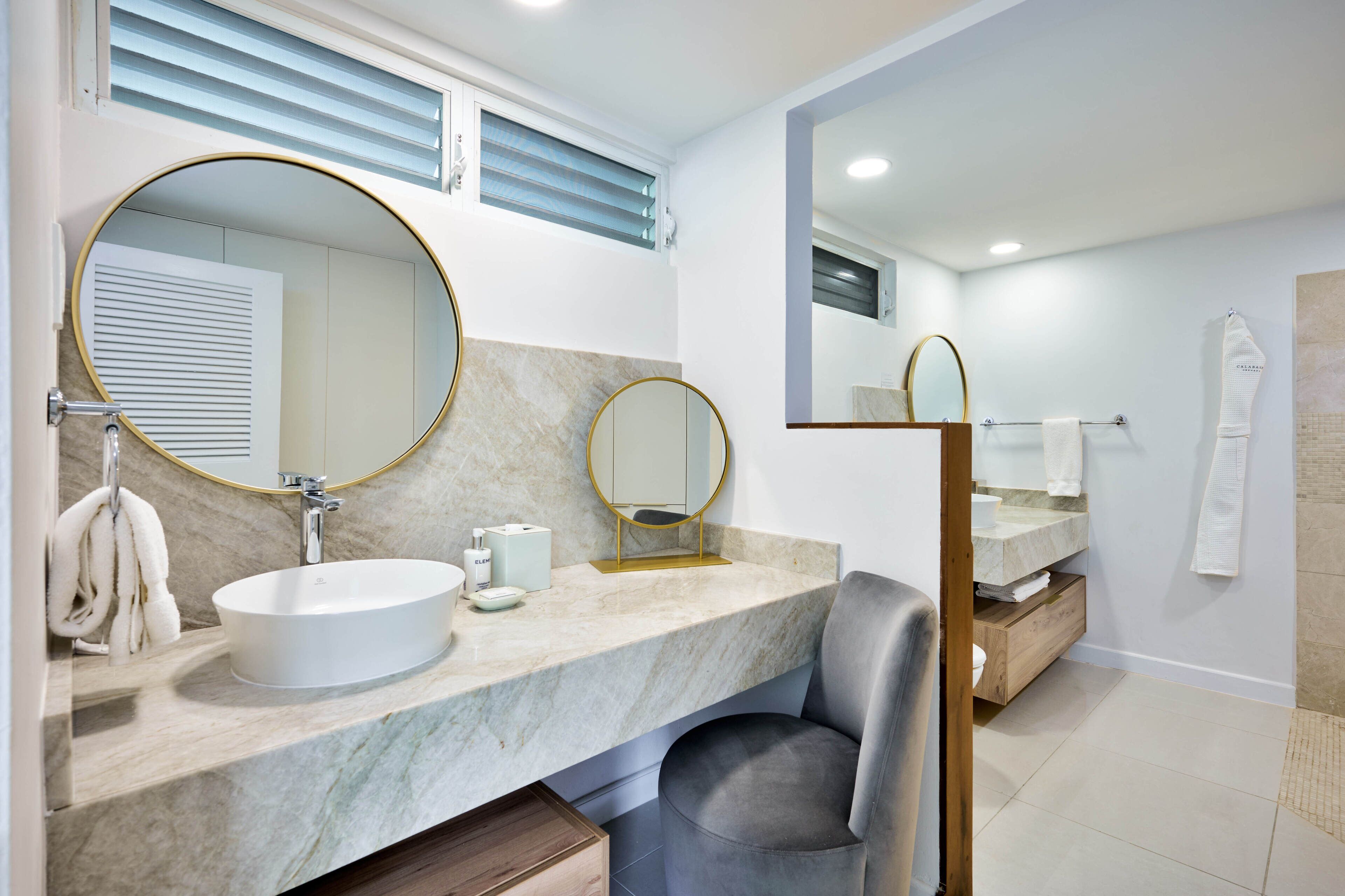 Un baño moderno con un espejo redondo grande, un lavamanos y un mueble de tocador con encimera de mármol.