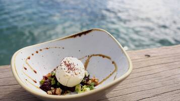 Un tazón de postre con una bola de helado, decorado con especias, sobre una superficie de madera con un cuerpo de agua desenfocado al fondo.
