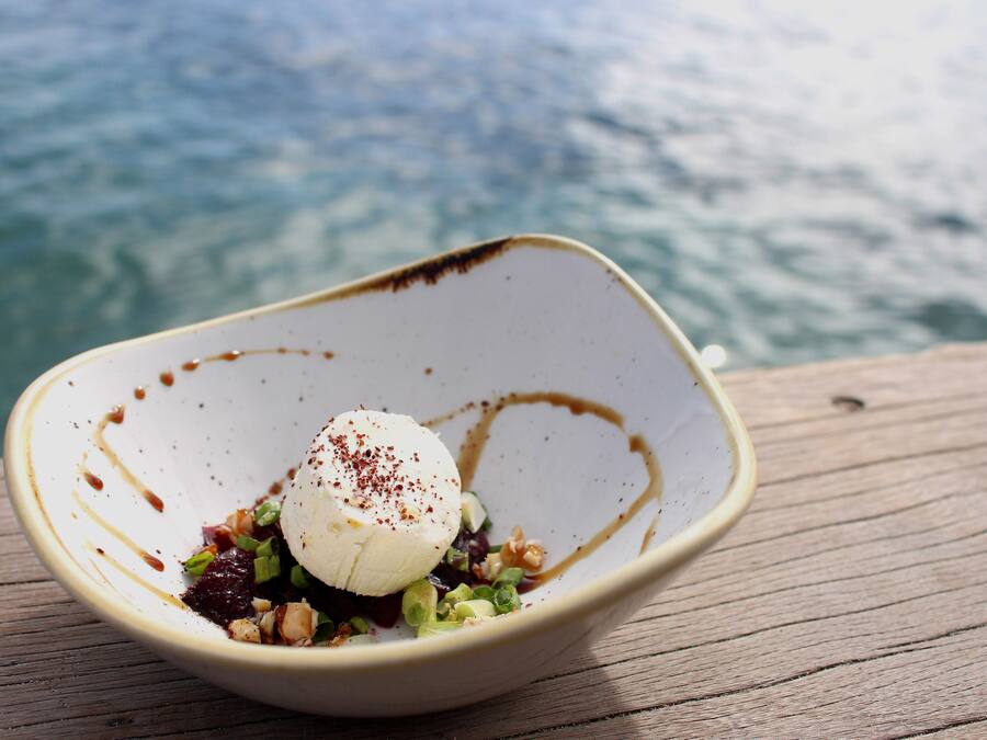 Un tazón de postre con una bola de helado, decorado con especias, sobre una superficie de madera con un cuerpo de agua desenfocado al fondo.