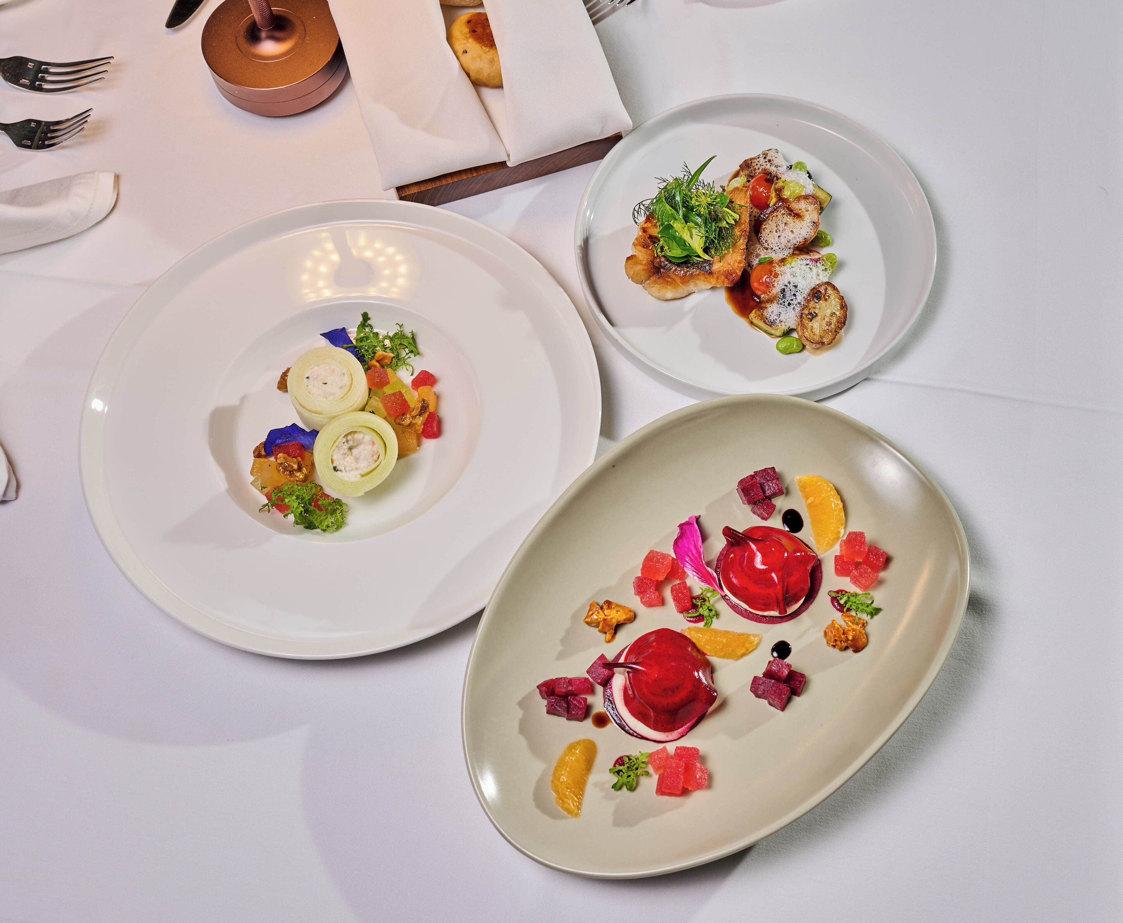 Three plates of food with various garnishes and a napkin with a utensil holder.