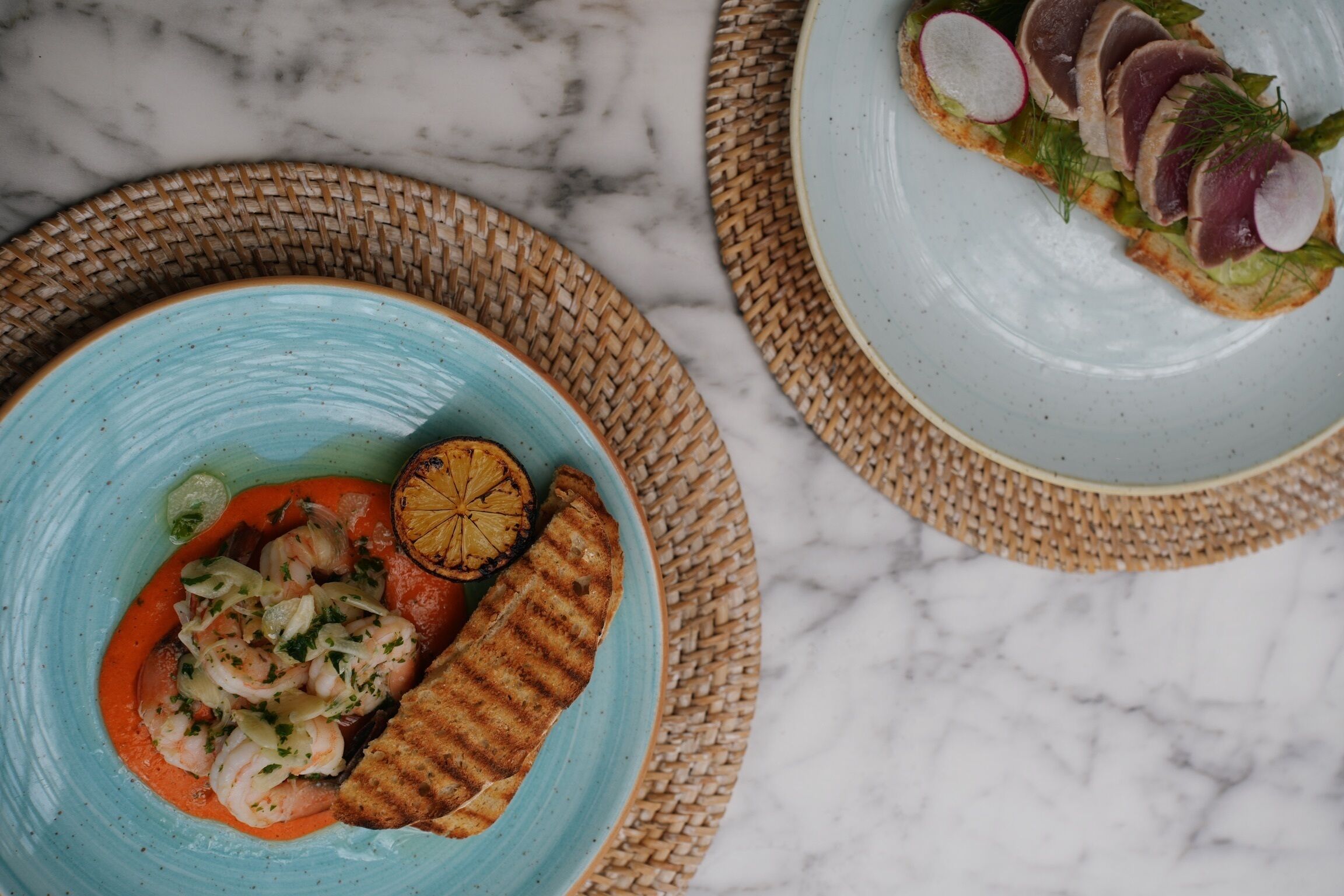 A table with a blue plate of food, a woven placemat, and a marble surface.