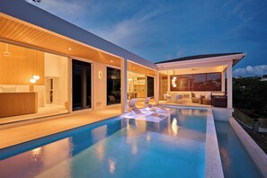 Una casa moderna con piscina, mobiliario de exterior y un patio cubierto.