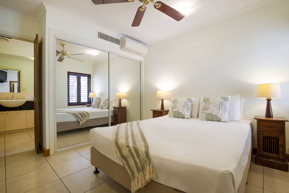 A bedroom with a bed, bedside lamps, a mirror, and a ceiling fan.