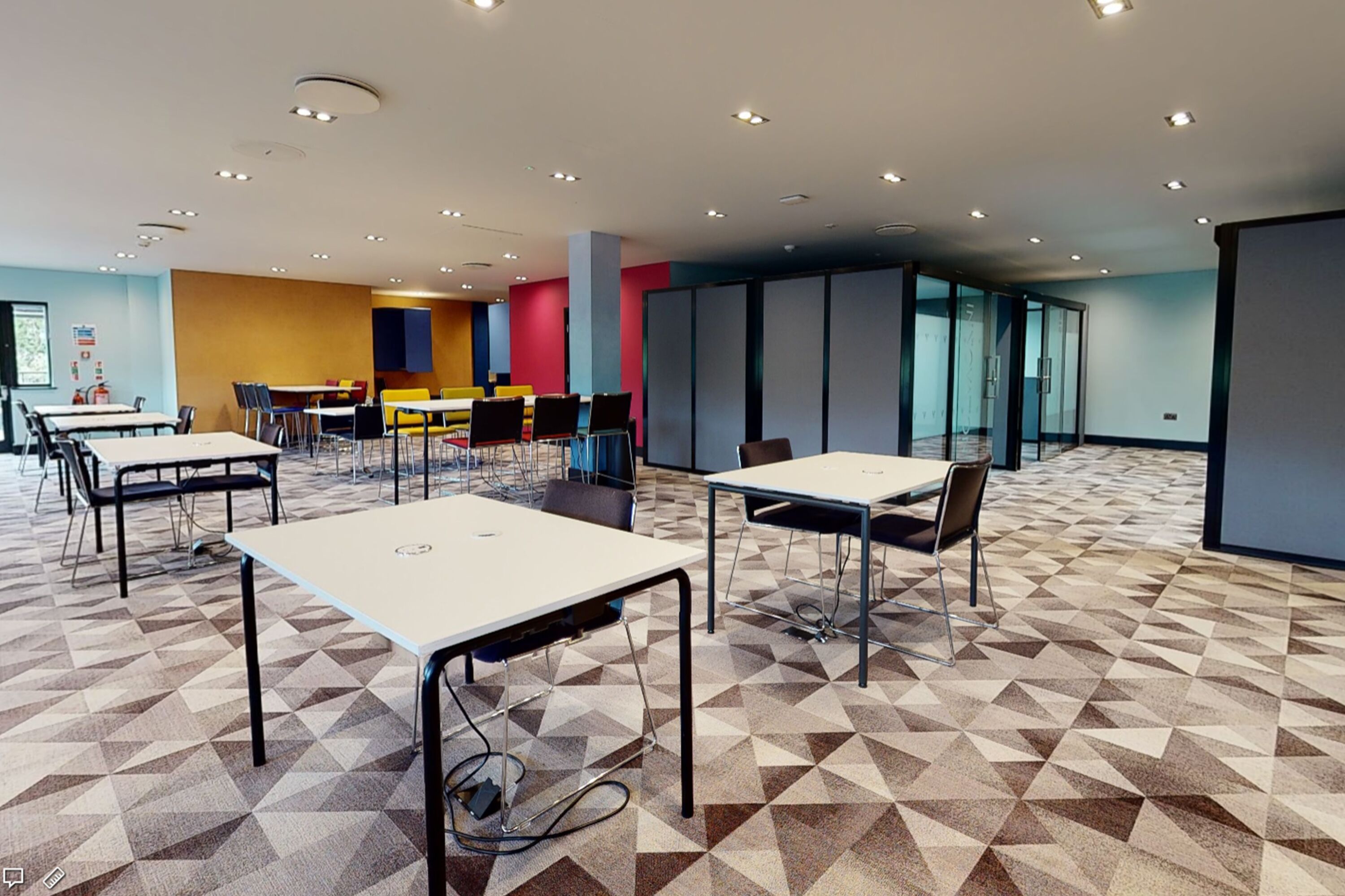 Une salle de conférence moderne dotée d’un tapis à motifs géométriques, de plusieurs tables et chaises, et d’une cloison en verre.