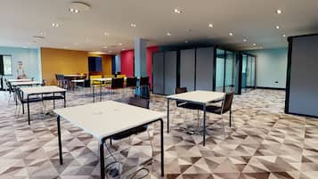 A modern conference room with geometric patterned carpet, multiple tables and chairs, and a glass partition wall.