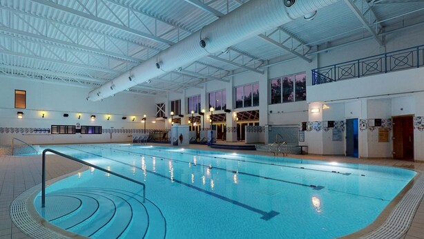Une piscine intérieure avec des lignes de démarcation bien visibles, un sol carrelé et un plafond haut laissant apparaître les conduits de ventilation.