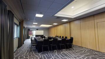 A conference room with a long table, chairs, a projector screen, and a carpeted floor.