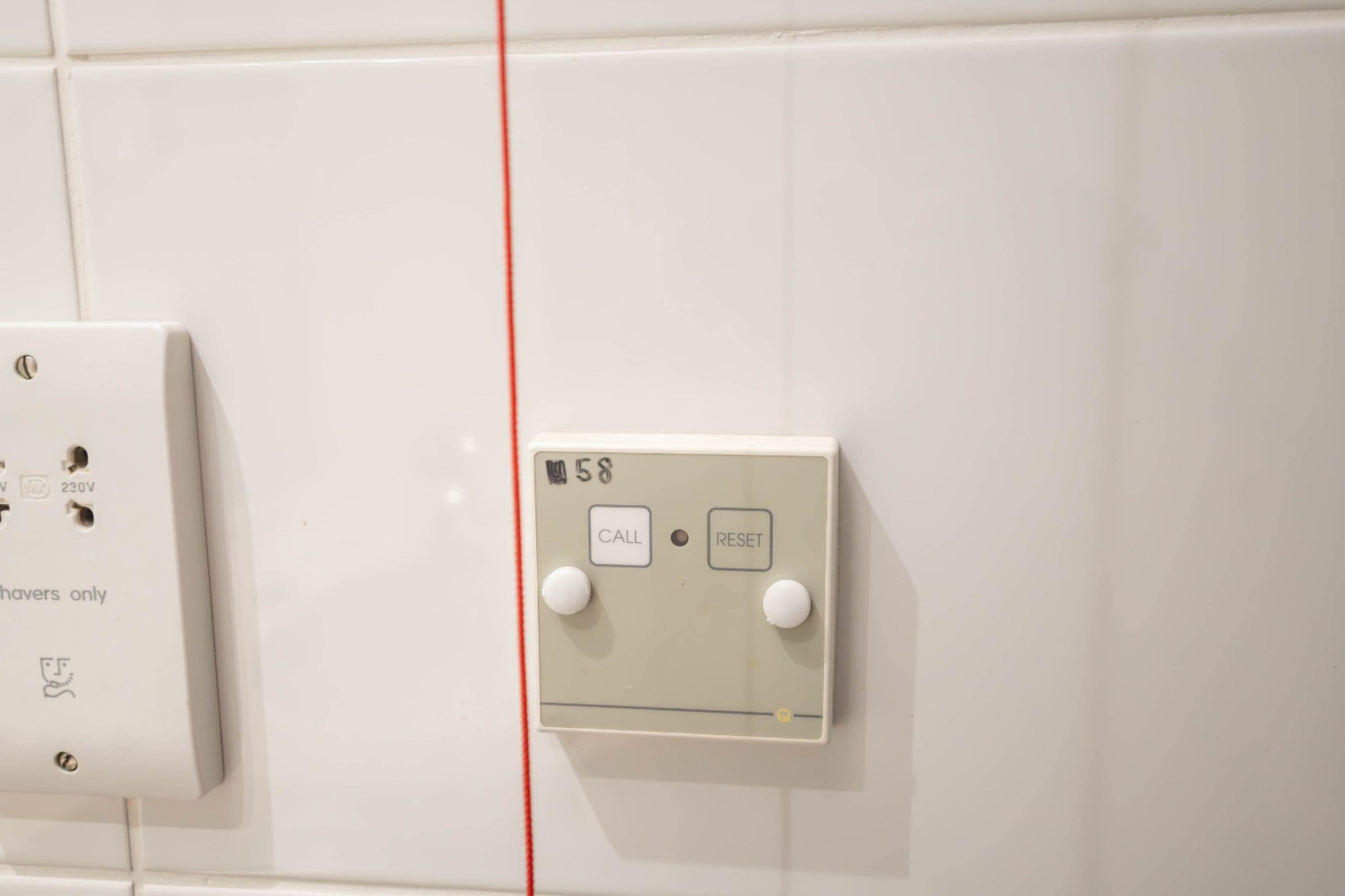 A wall-mounted electrical panel with two switches labeled 'CALL' and 'RESET' and a red cable running vertically.