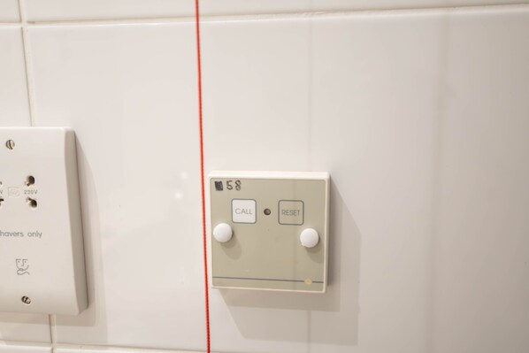 Un cuadro eléctrico fijado a la pared con dos interruptores etiquetados 'CALL' y 'RESET', y un cable rojo que baja verticalmente.