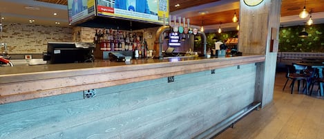 A bar area with a wooden counter, a mounted television displaying a news program, and a clock on the wall.