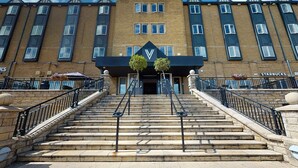 Un bâtiment orné d’un logo en forme de « V » bien visible, avec un escalier menant à l’entrée et une enseigne Starbucks sur la droite.