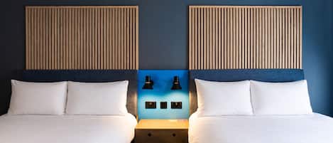 A double room with two beds, a nightstand, two wall-mounted lamps, and a blue accent wall.