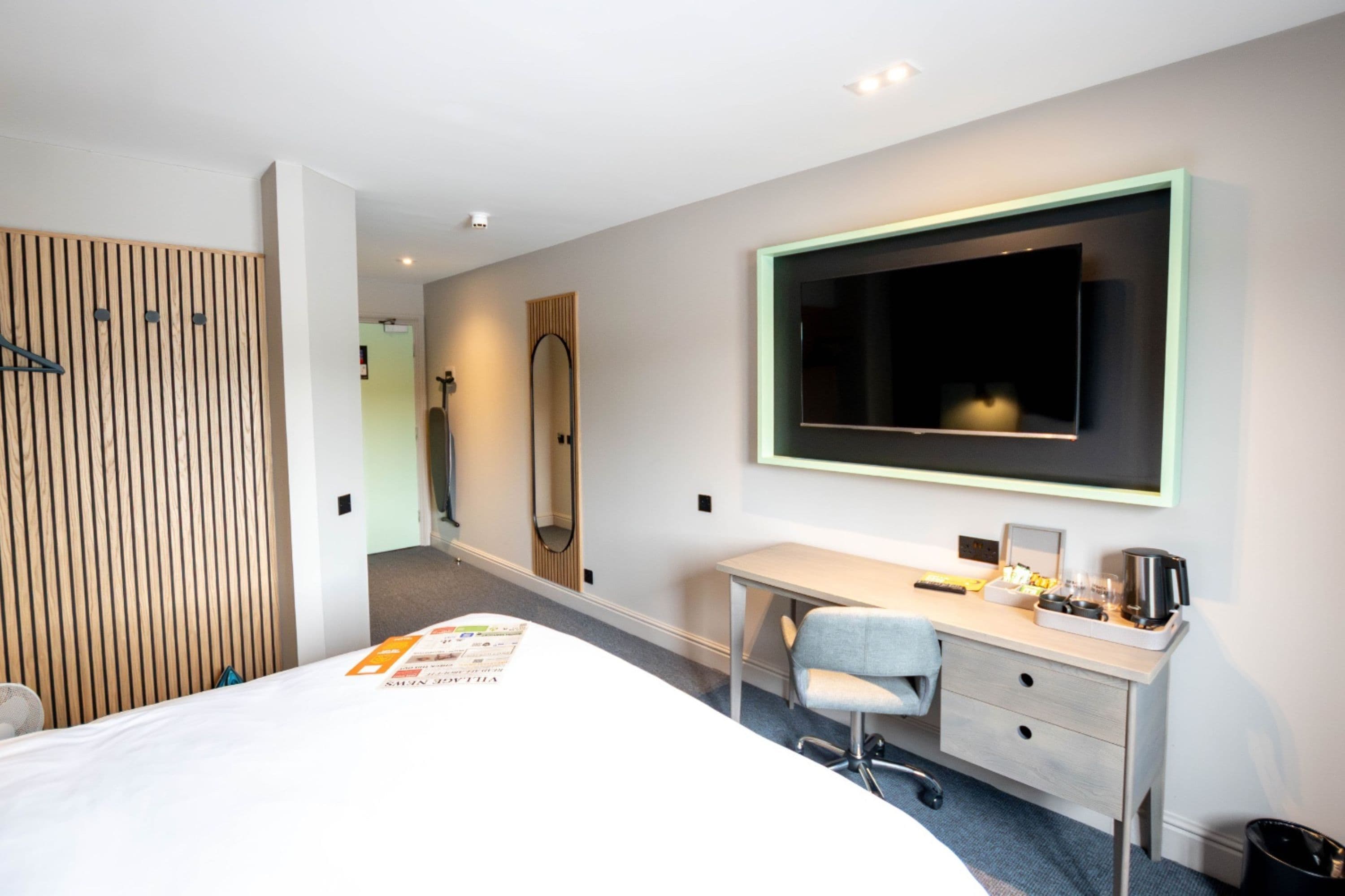A hotel room with a bed, a desk with a chair, a large mirror, and a television.
