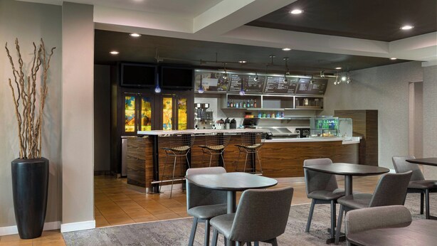 Un restaurante moderno con zona de bar, asientos y un gran jarrón con ramas.