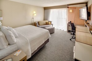Una habitación de hotel con una cama grande, un escritorio con una silla, un televisor y una lámpara.